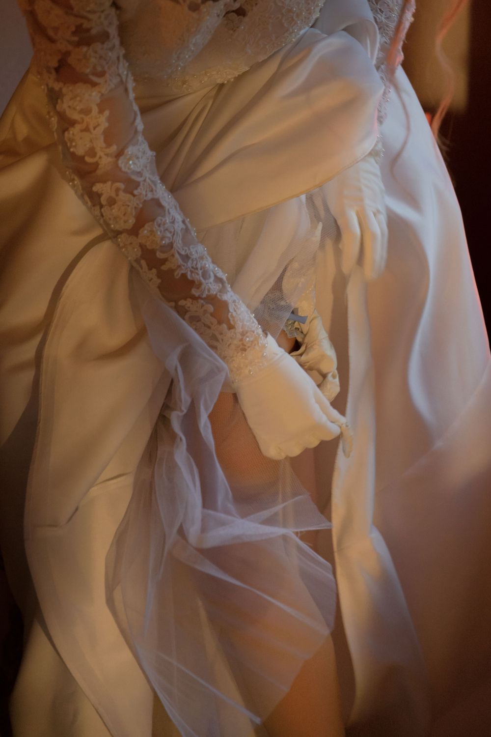 Close-up detail of white wedding dress showing intricate lace sleeve and flowing fabric.