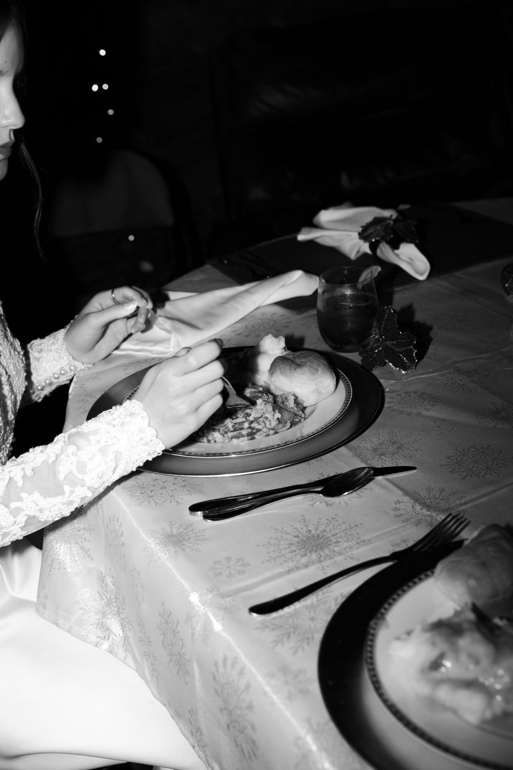 Black and white photo of elegant table setting with formal dinnerware and lace details.