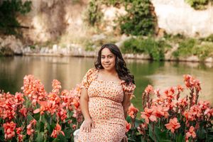 Polka dot dress harmonizes with blooming coral iris flowers beside scenic lake on sunny spring day.