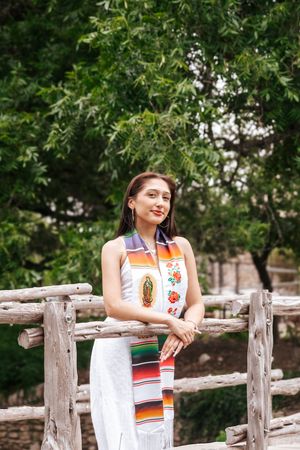 A person in a Mexican-style serape stands on a rustic wooden bridge surrounded by lush green foliage.