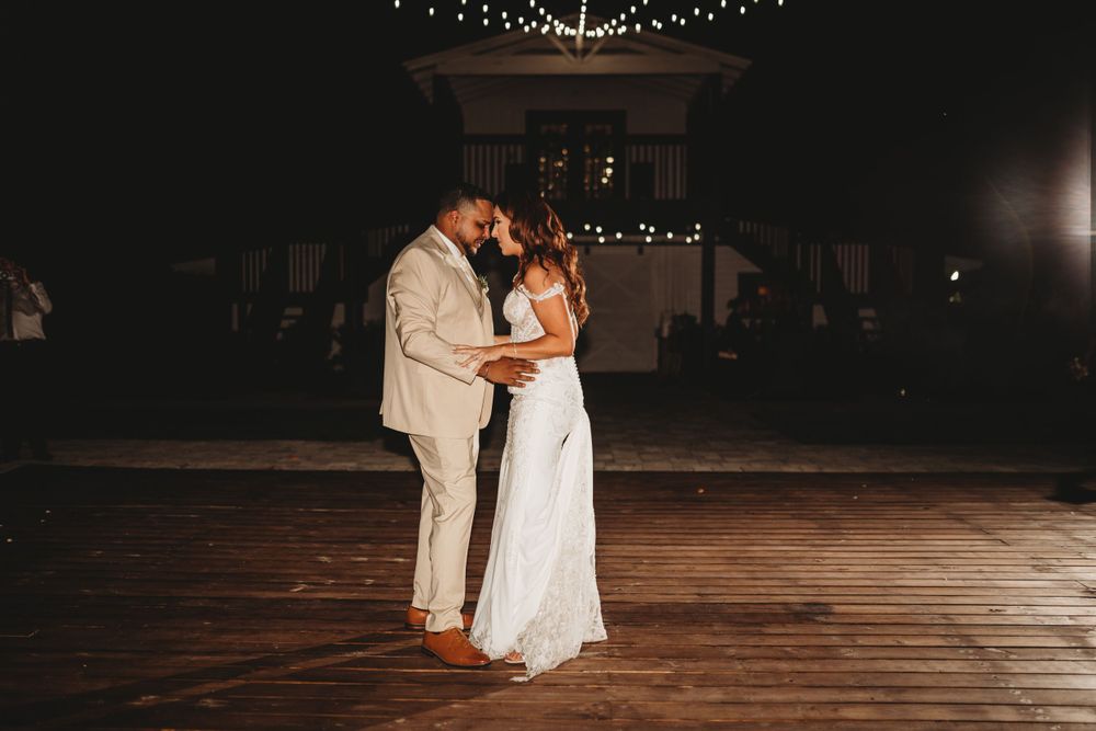 Newlyweds share intimate first dance on wooden floor under string lights.