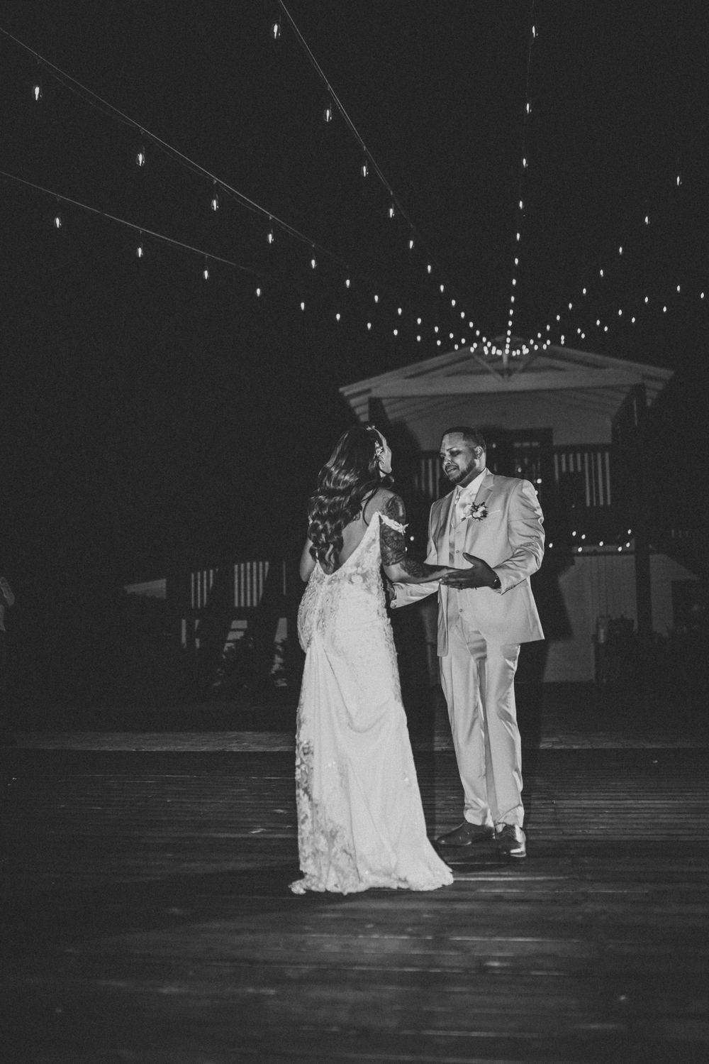 Couple dancing under twinkling lights at an outdoor wedding reception at night.