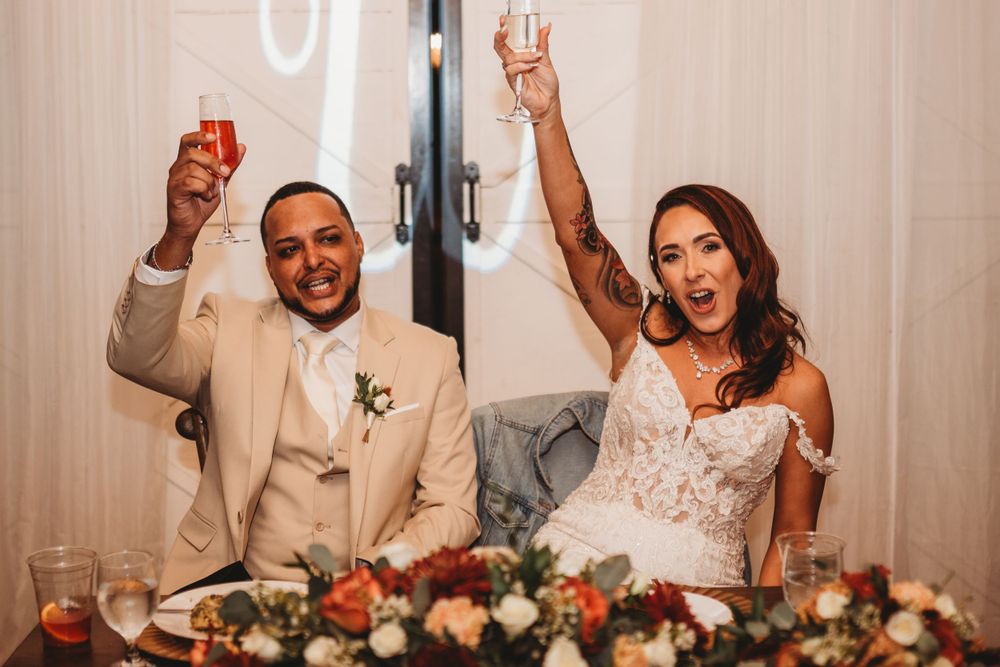 Wedding couple celebrates with raised glasses during reception dinner.
