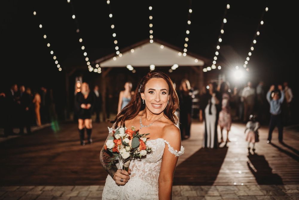 Bride holding bouquet on illuminated outdoor deck during evening reception.