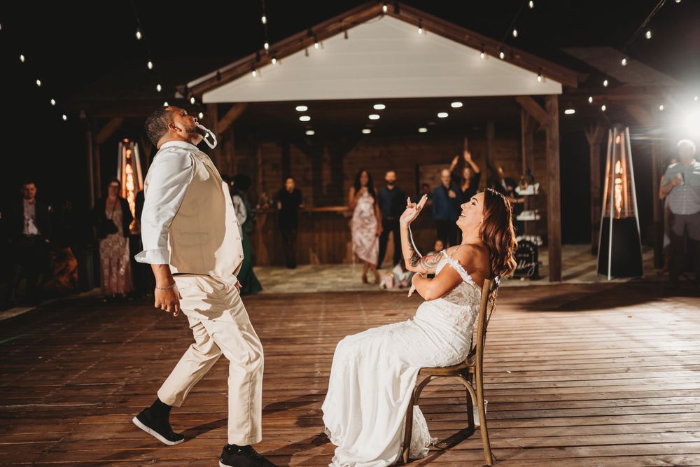Wedding reception scene with couple performing traditional garter removal on wooden deck.