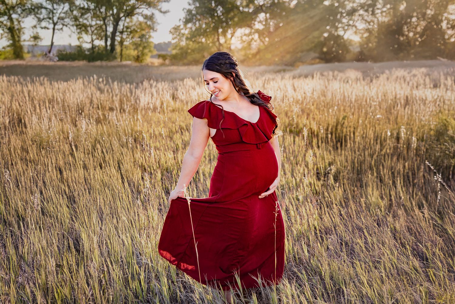Expecting mother in red gown during golden hour field session captured by luxury maternity photographer in Denver.
