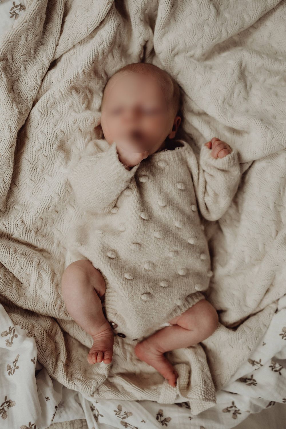 Baby wearing dotted onesie resting on cream-colored textured blanket.