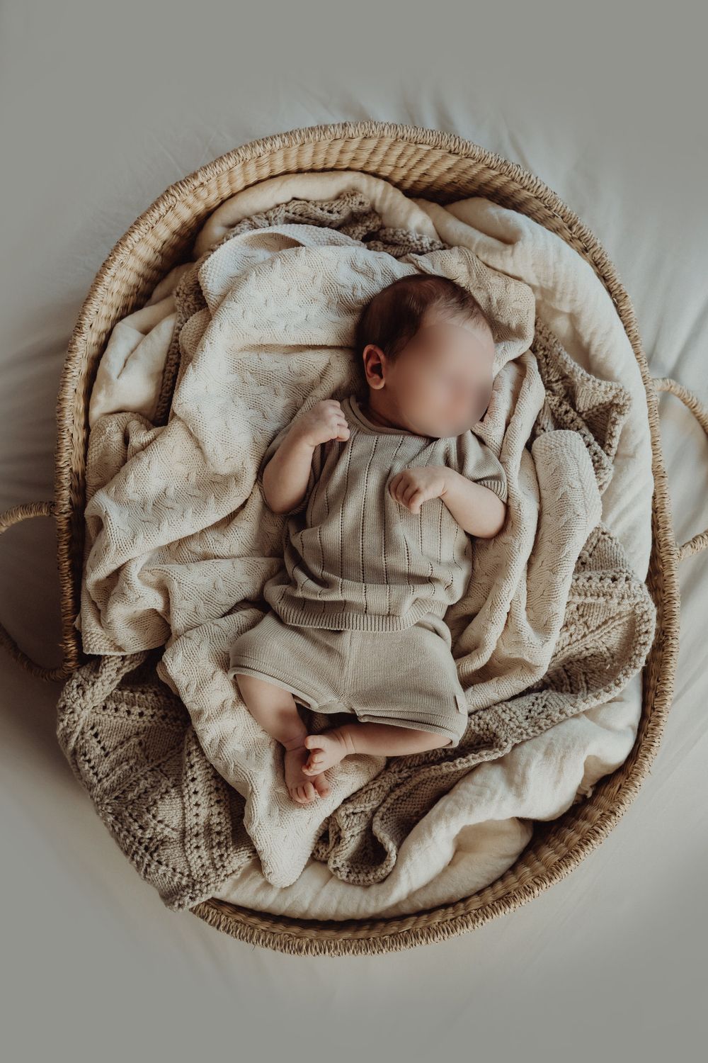 Newborn sleeping peacefully in round wicker basket with soft textured linens.