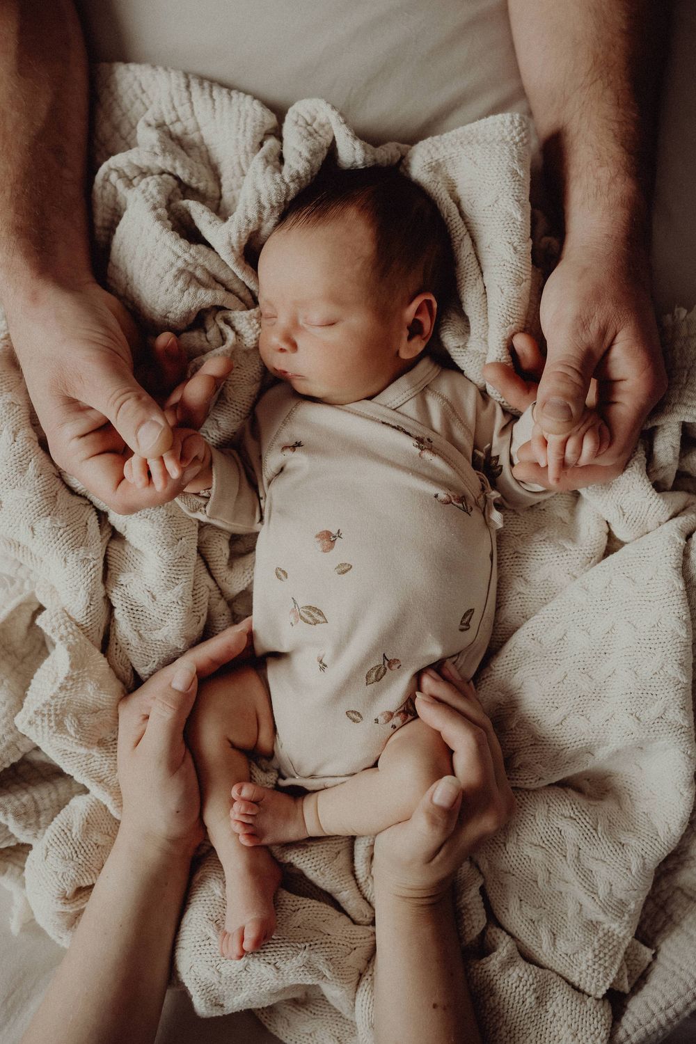 Newborn baby sleeping peacefully on textured blanket with hands tenderly holding.
