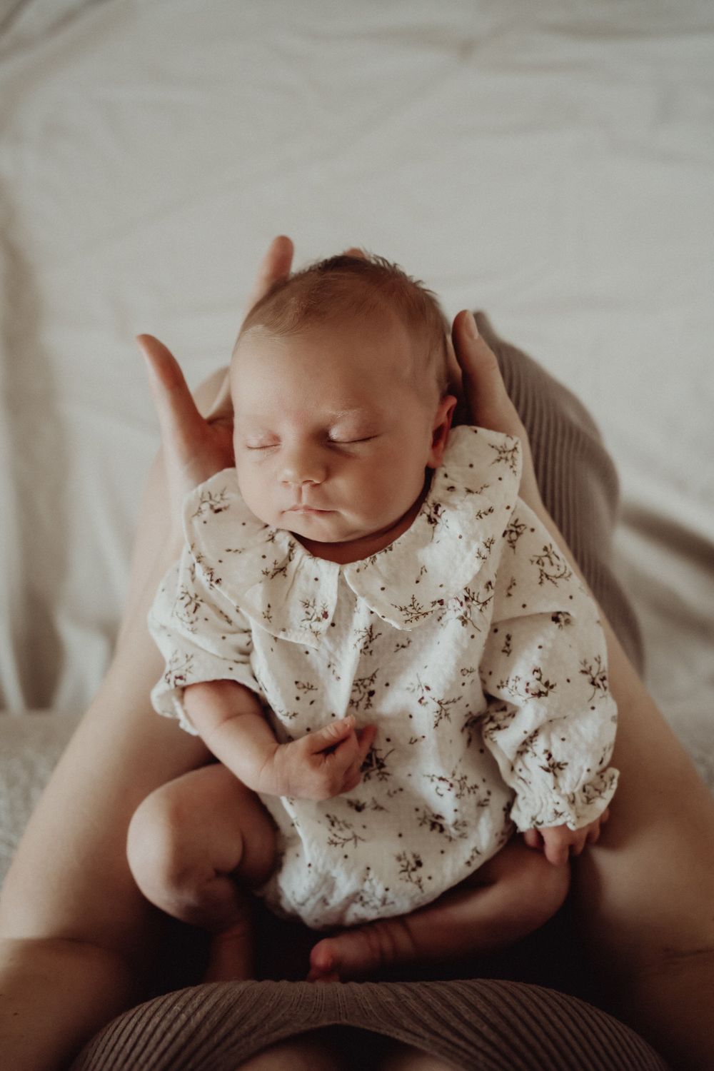 Sleeping infant in floral dress cradled gently.