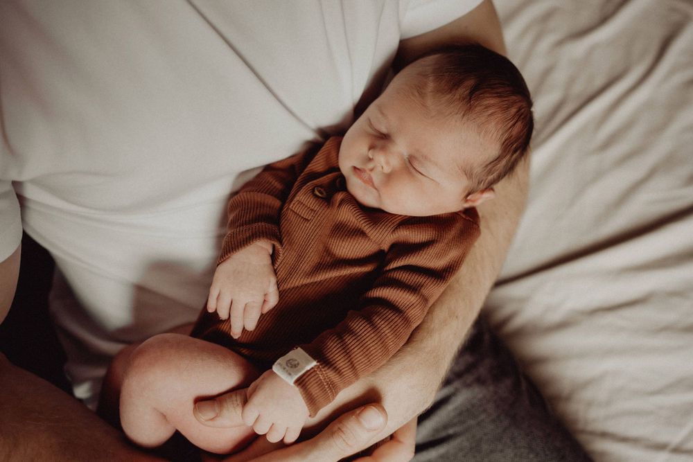 Peaceful newborn in brown outfit resting on white fabric.