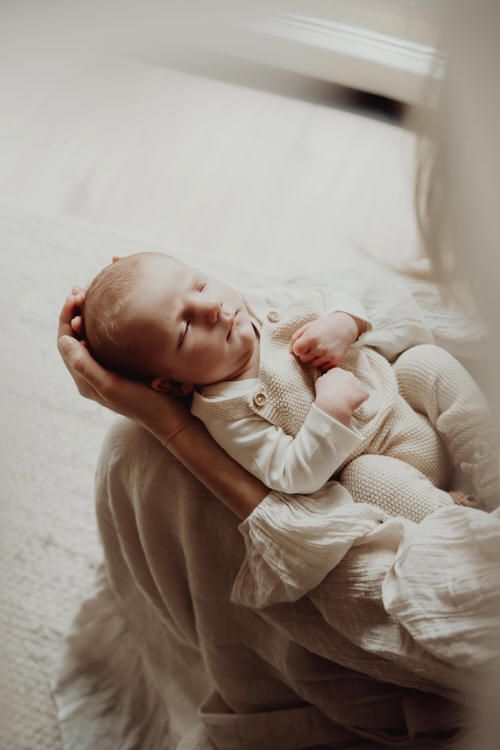 Sleeping baby in white outfit being cradled against soft fabric.