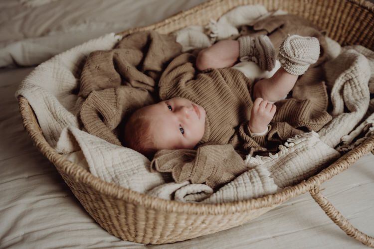 Baby resting peacefully in woven basket surrounded by neutral toned blankets.