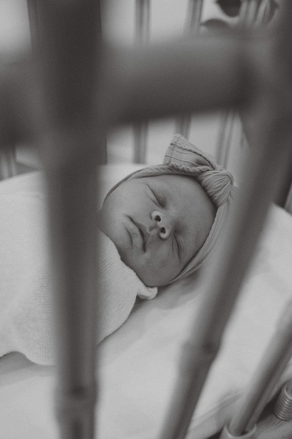 A sleeping baby lies peacefully in a white crib viewed through the slats of the railing.