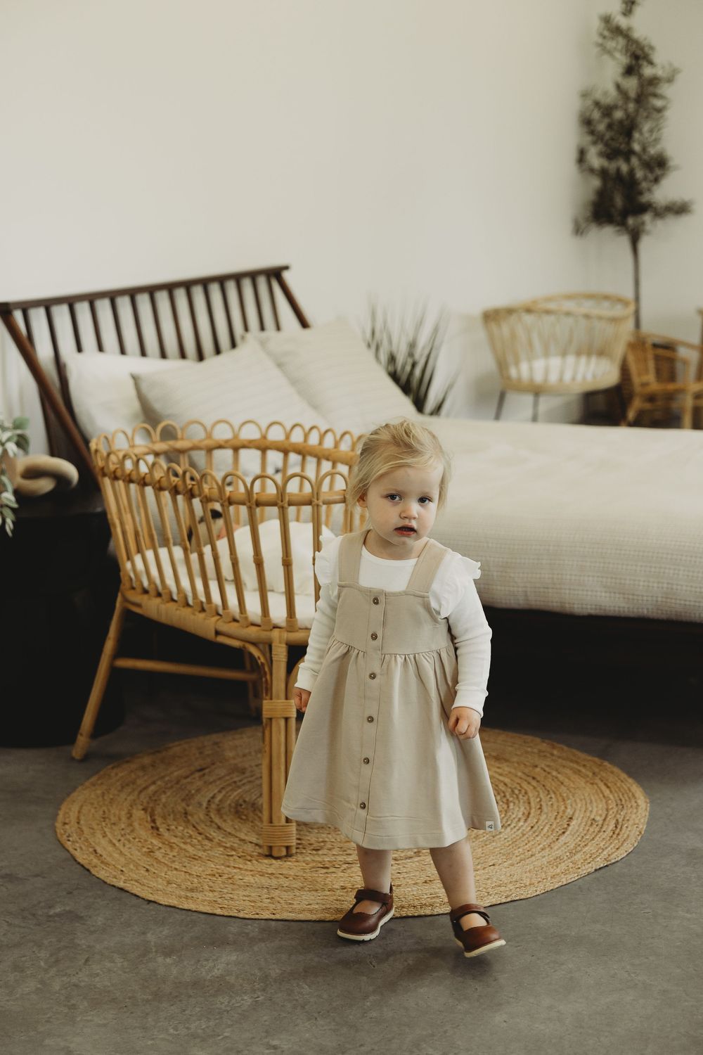 A series of photos showing a small child in a cream-colored outfit playing near a rattan bench on a round jute rug.