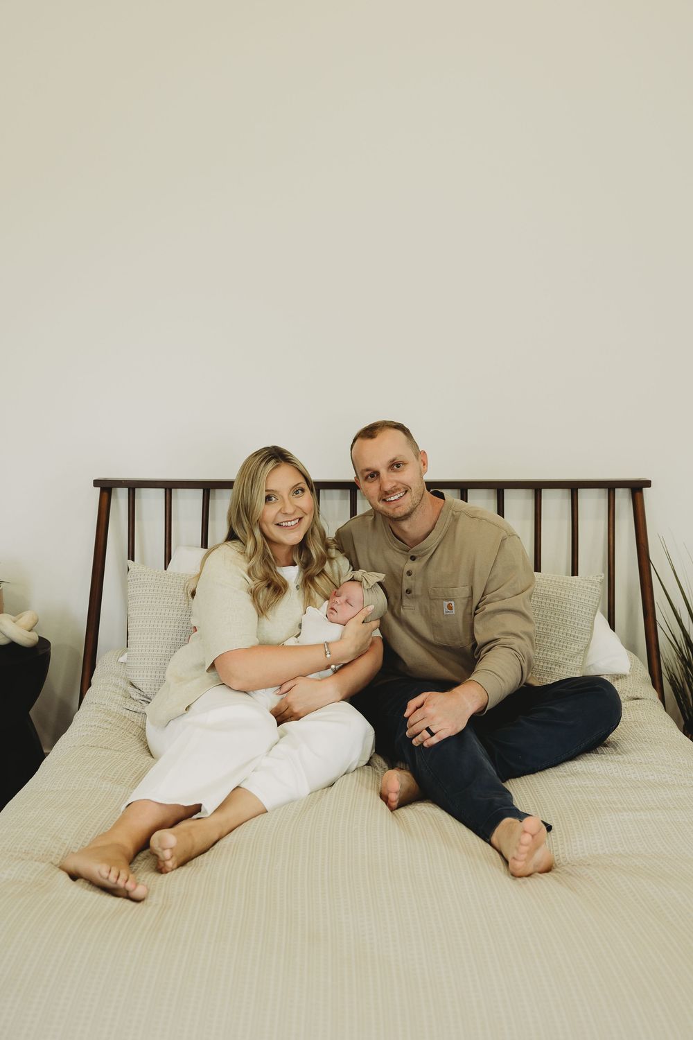 A couple relaxes together on a white bed wearing casual clothing in a minimalist setting.