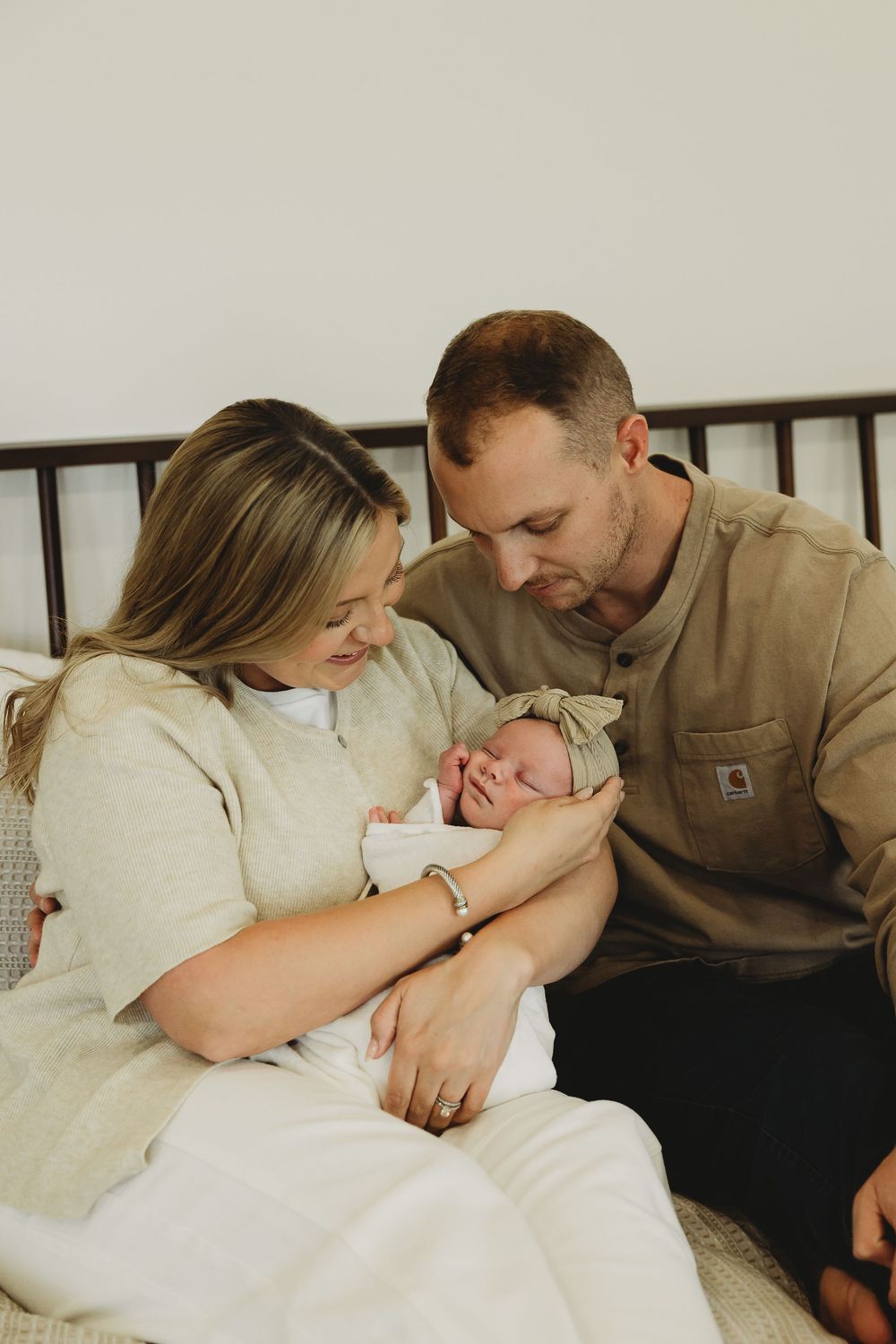 A tender family moment captured in a series of intimate photos showing parents cuddling with their newborn baby on a bed.