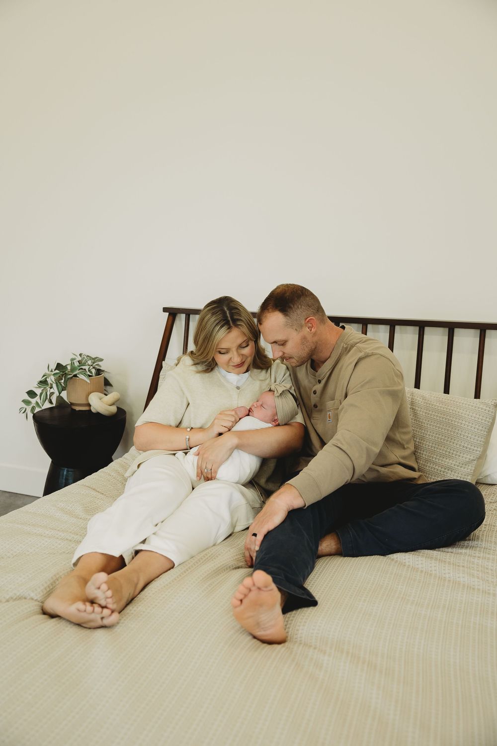 A couple sits together on a bed with white linens, wearing casual clothing while sharing an intimate moment.