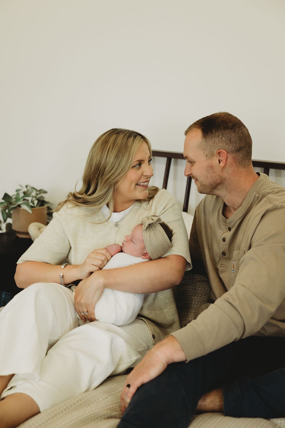 Family lounging together on dark couch with newborn baby in intimate lifestyle photography series.