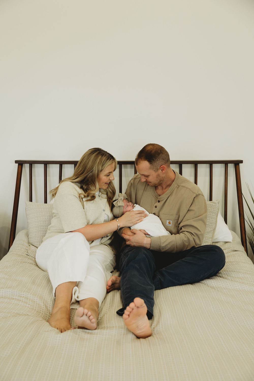 Family lying together on white bedding while sharing tender moments with their newborn baby.
