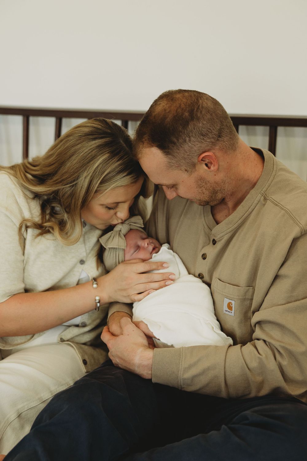 Parents in casual attire share intimate bonding moments with their newborn on a white bed.