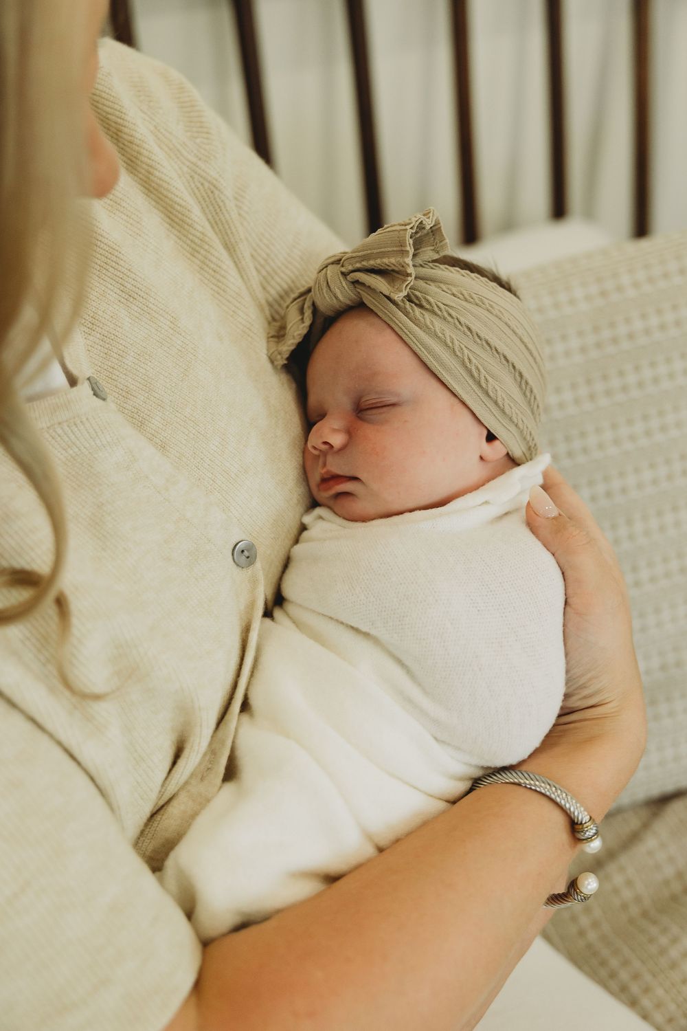 A sleeping newborn baby in a white onesie and beige hat rests peacefully in a crib.