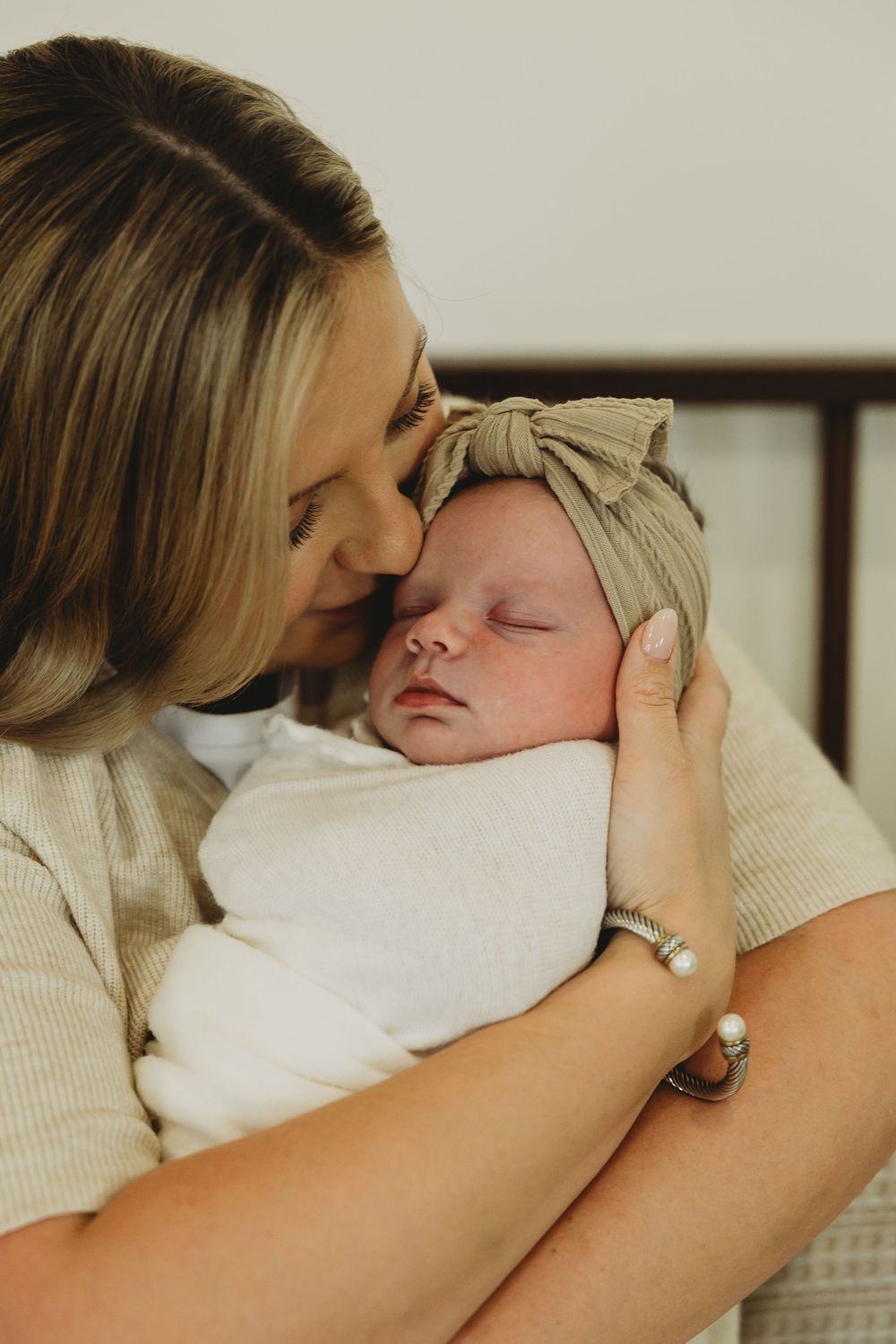 A tender moment as a parent cradles a sleeping newborn wearing a beige hat and white clothing.