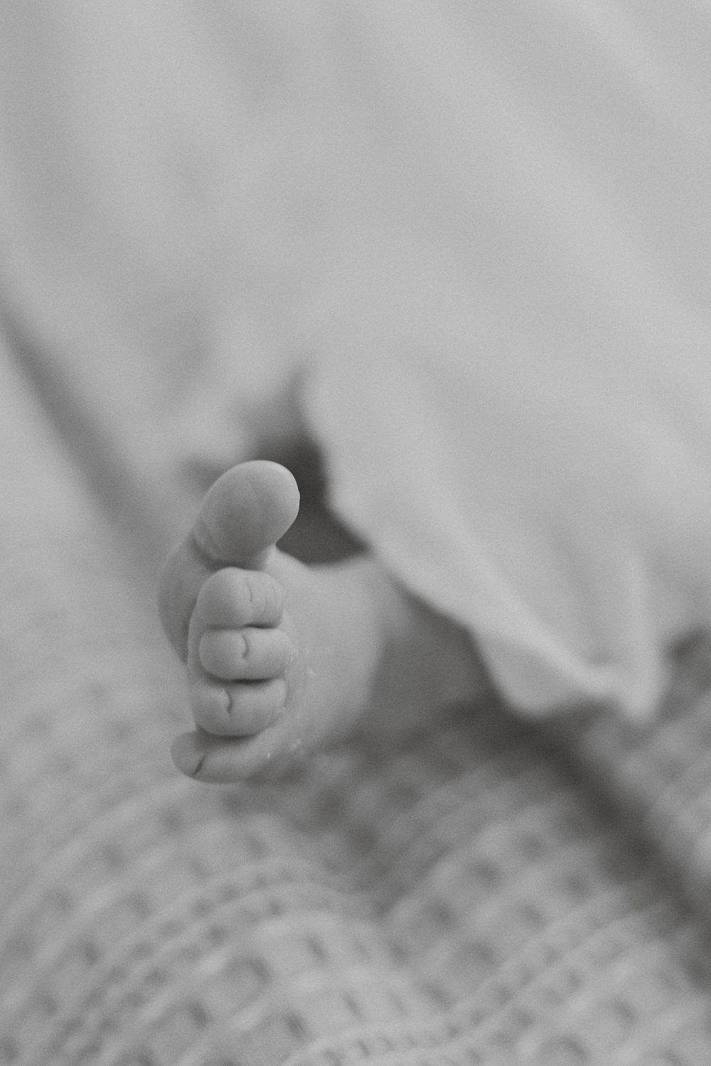 Close-up black and white photo of a tiny baby foot resting on textured fabric.
