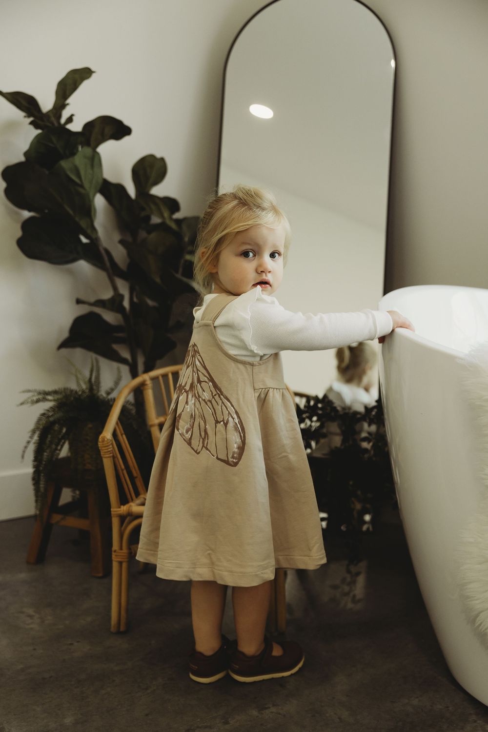 A toddler in a beige dress explores a modern interior space with potted plants and curved white walls.