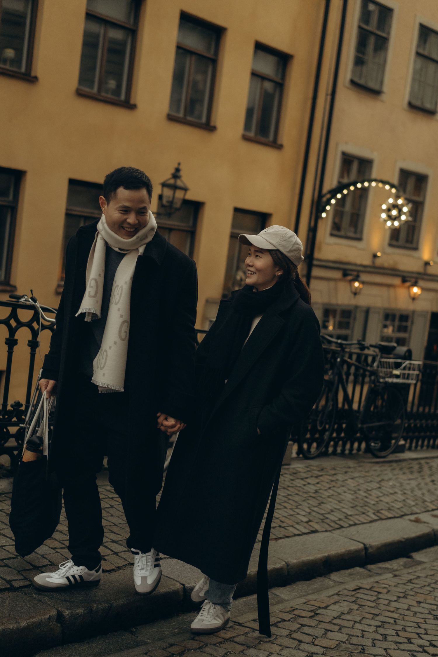 couple holding hands and walking through Christmas Gamla Stan while being captured by documentary couple photographer in Stockholm