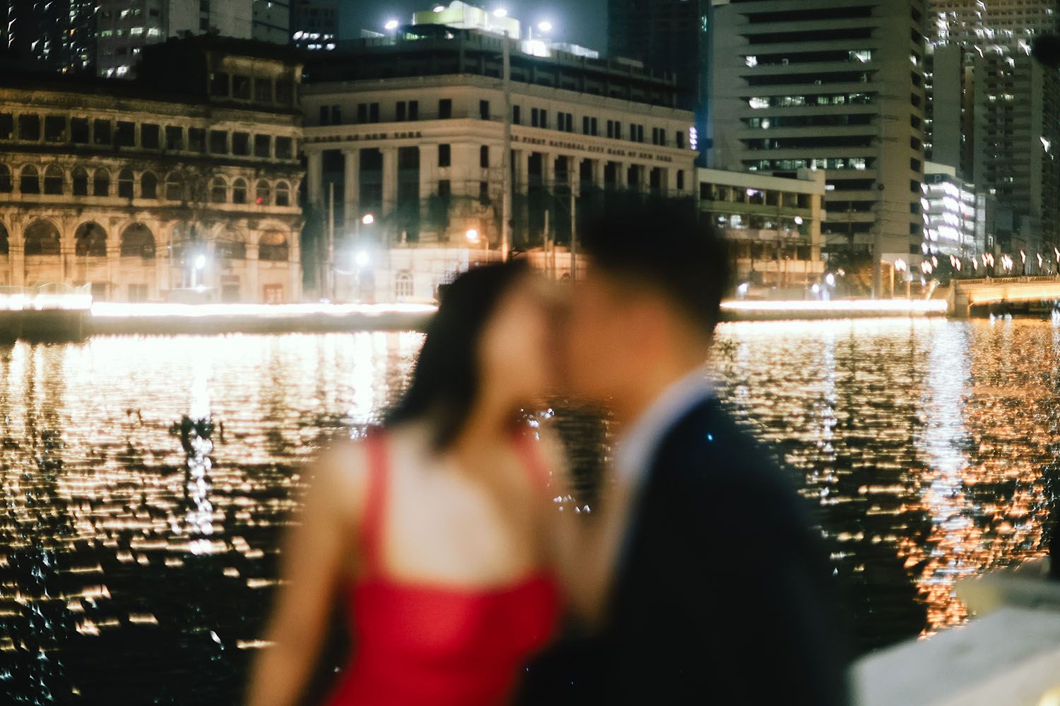 Silhouettes of couples dance against a glittering cityscape backdrop at night with twinkling lights reflecting on water.