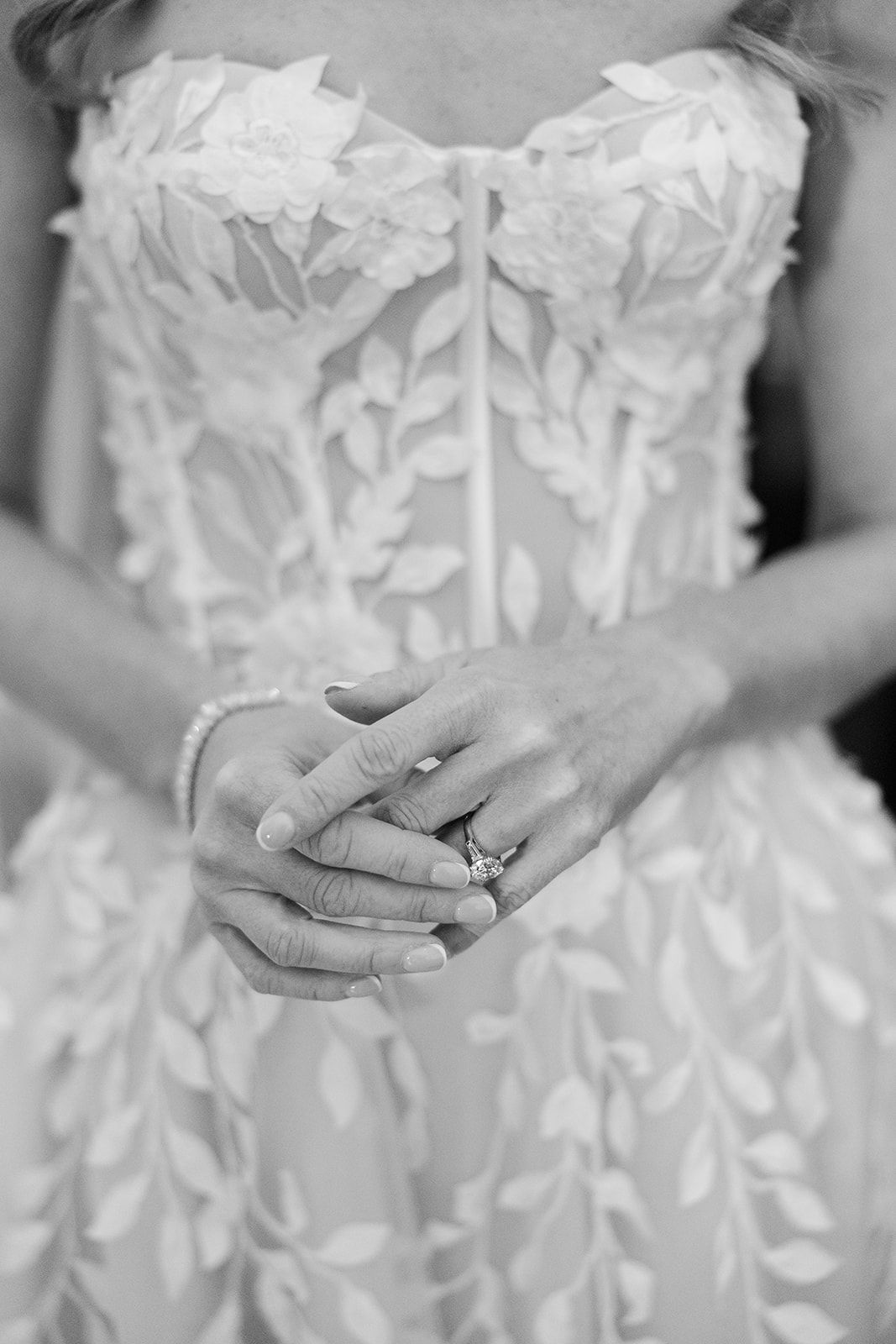 A series of black and white photos showing hands holding engagement rings against white lace wedding dresses.