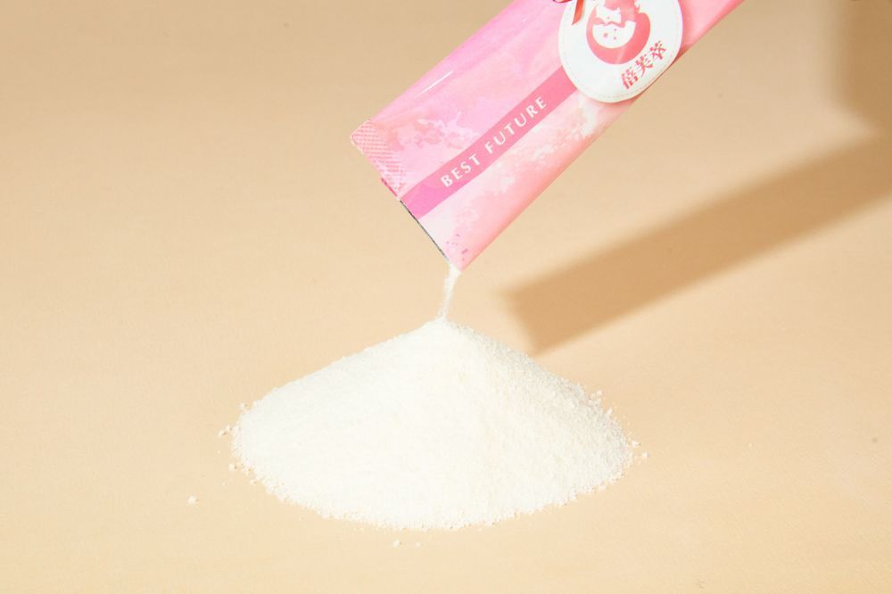 A pink and white frosted cupcake with sprinkles sits on a light colored surface in soft lighting.
