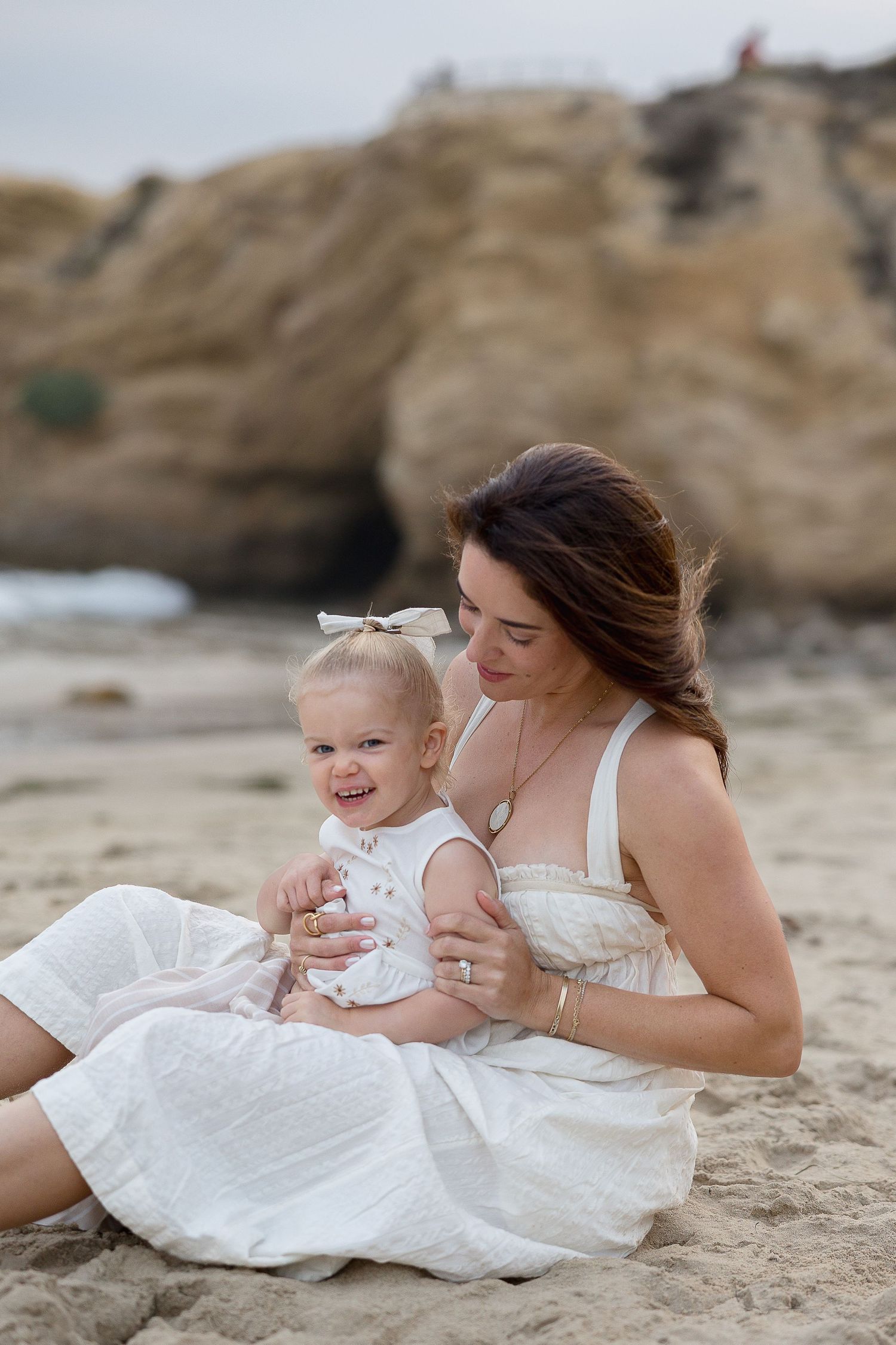Beach family photo of mom holding their child sitting at Crystal Cove cliffs