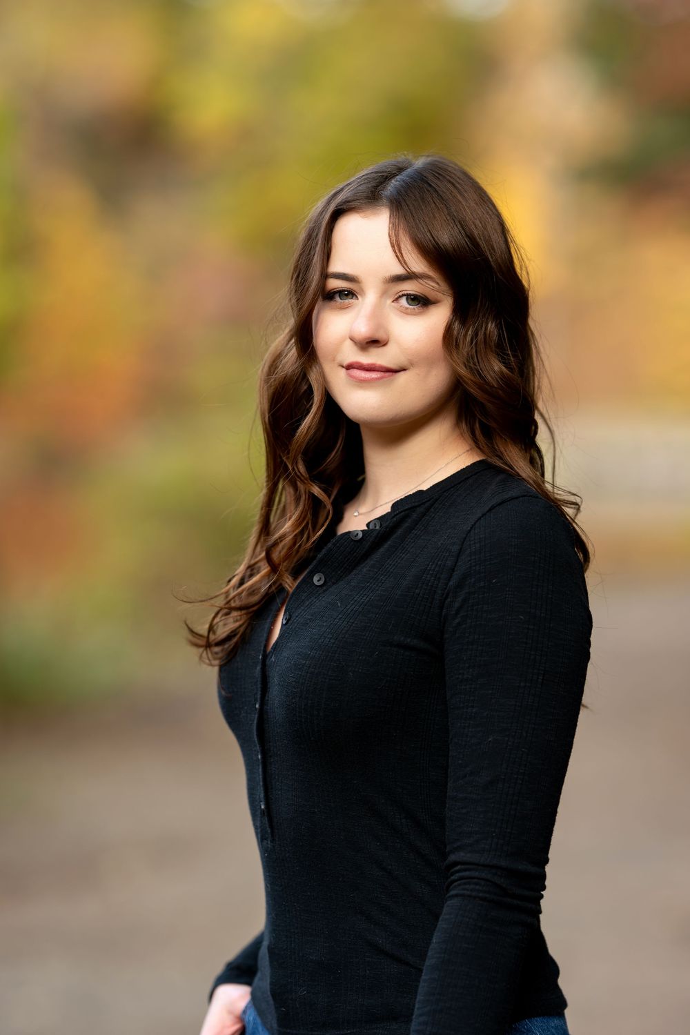 Brunette woman in black cardigan smiles softly during fall outdoor portrait session.