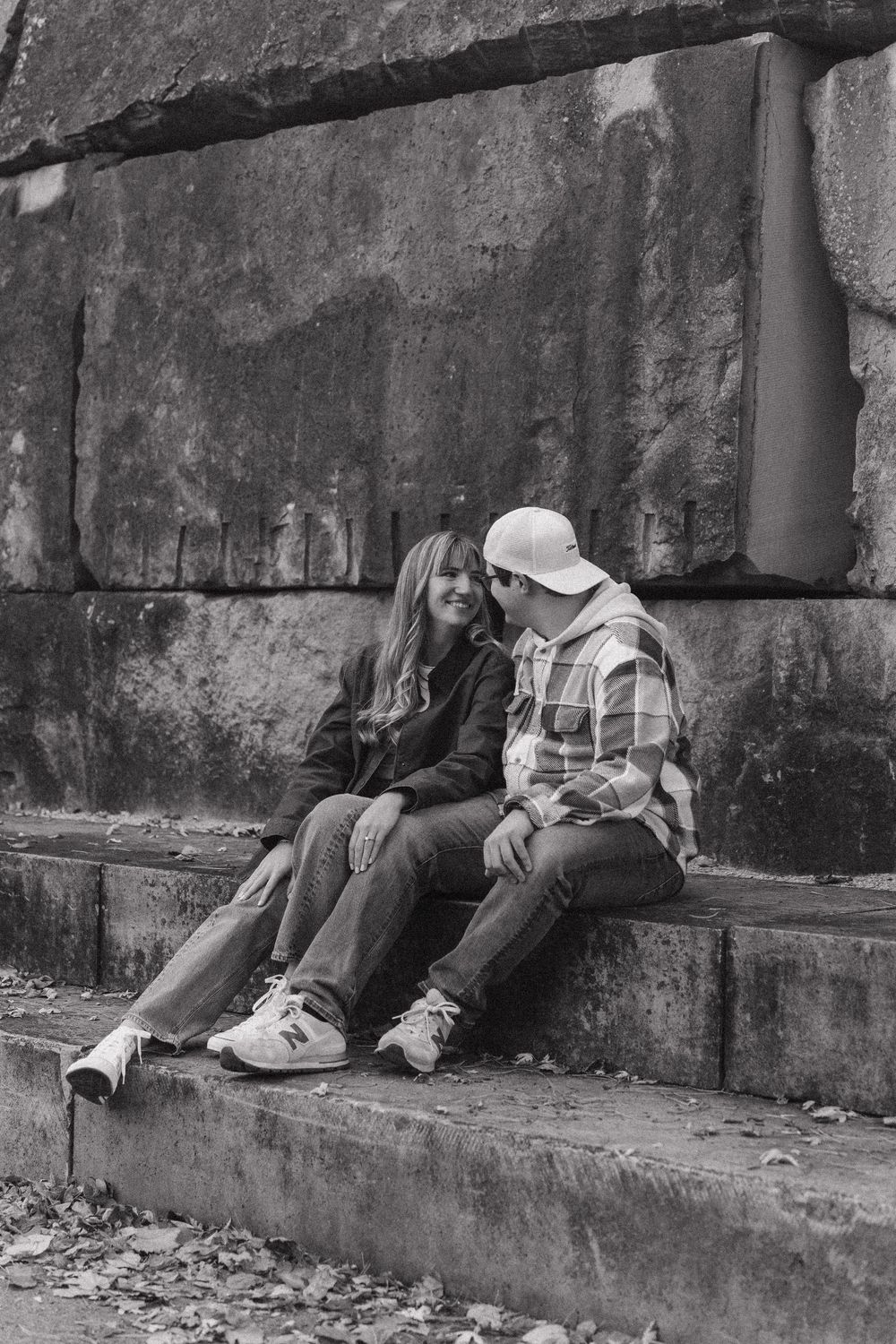 People sit on concrete steps in a black and white urban scene with a weathered wall behind them.