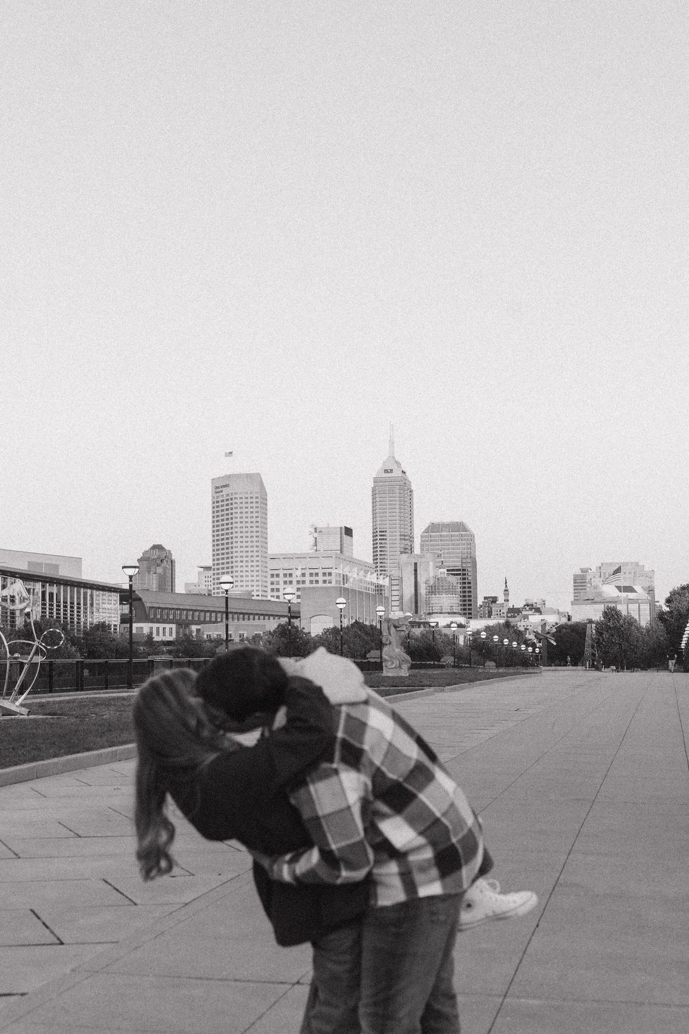 Black and white photo of a couple embracing with Indianapolis city skyline in the background.