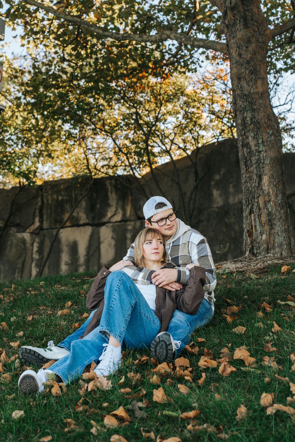Couple relaxing with their dog on a grassy hill covered in fallen autumn leaves on a sunny afternoon.