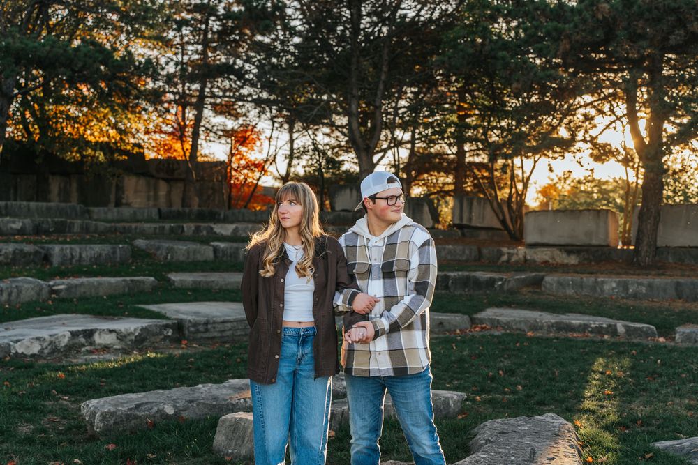 A couple poses for engagement photos in a rustic outdoor setting during golden hour sunset.