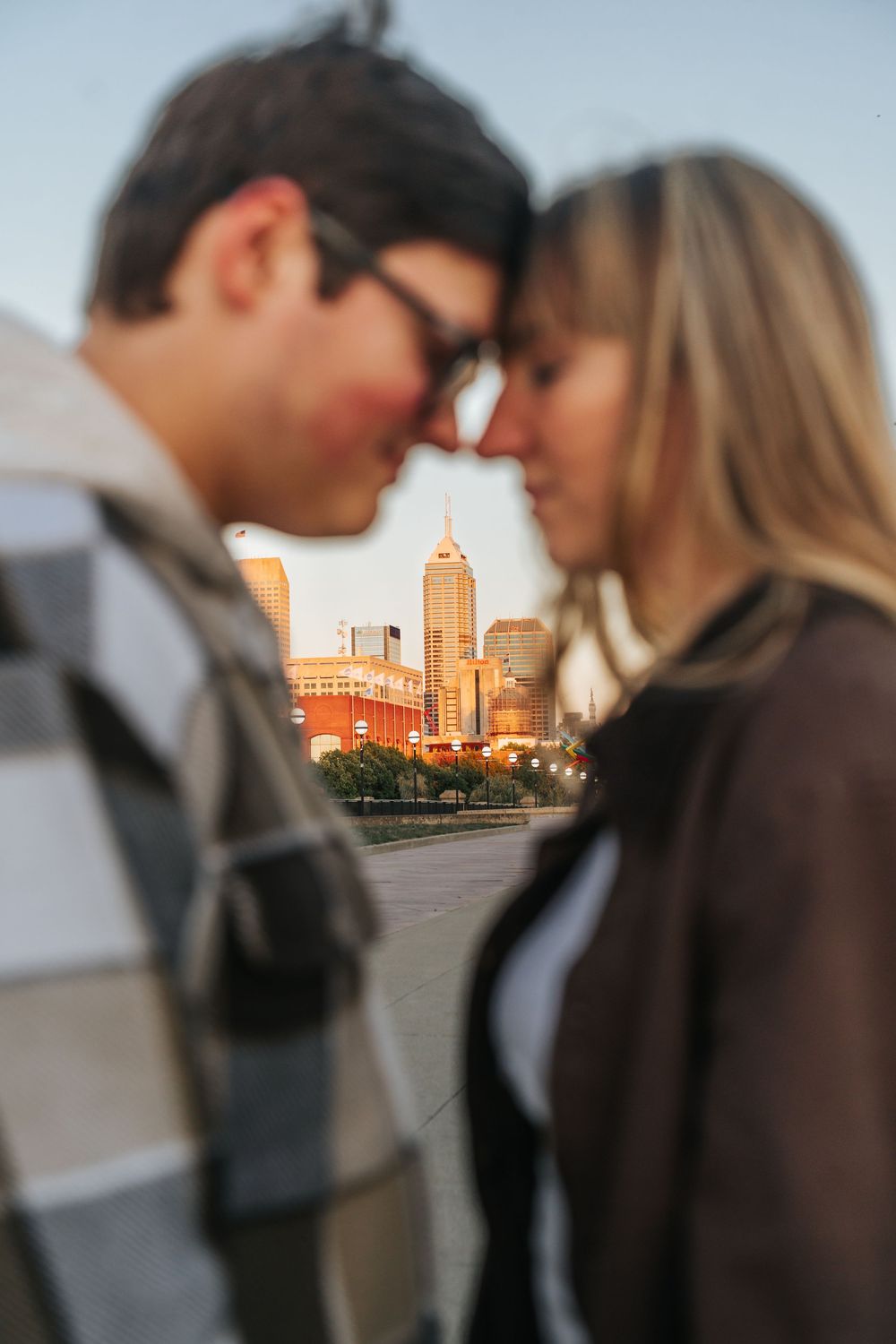 A couple shares an intimate moment at sunset with city buildings silhouetted in the warm golden light.