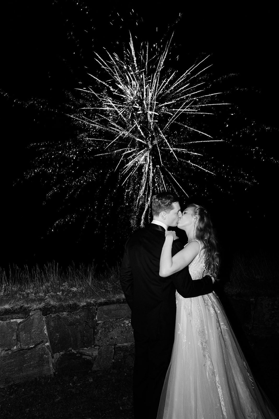Silhouetted couple embracing under dramatic fireworks display against dark night sky background.