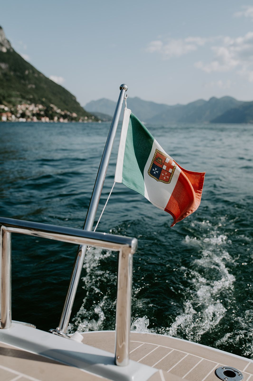 Italian flag waving on a boat with mountains and lake scenery in the background.