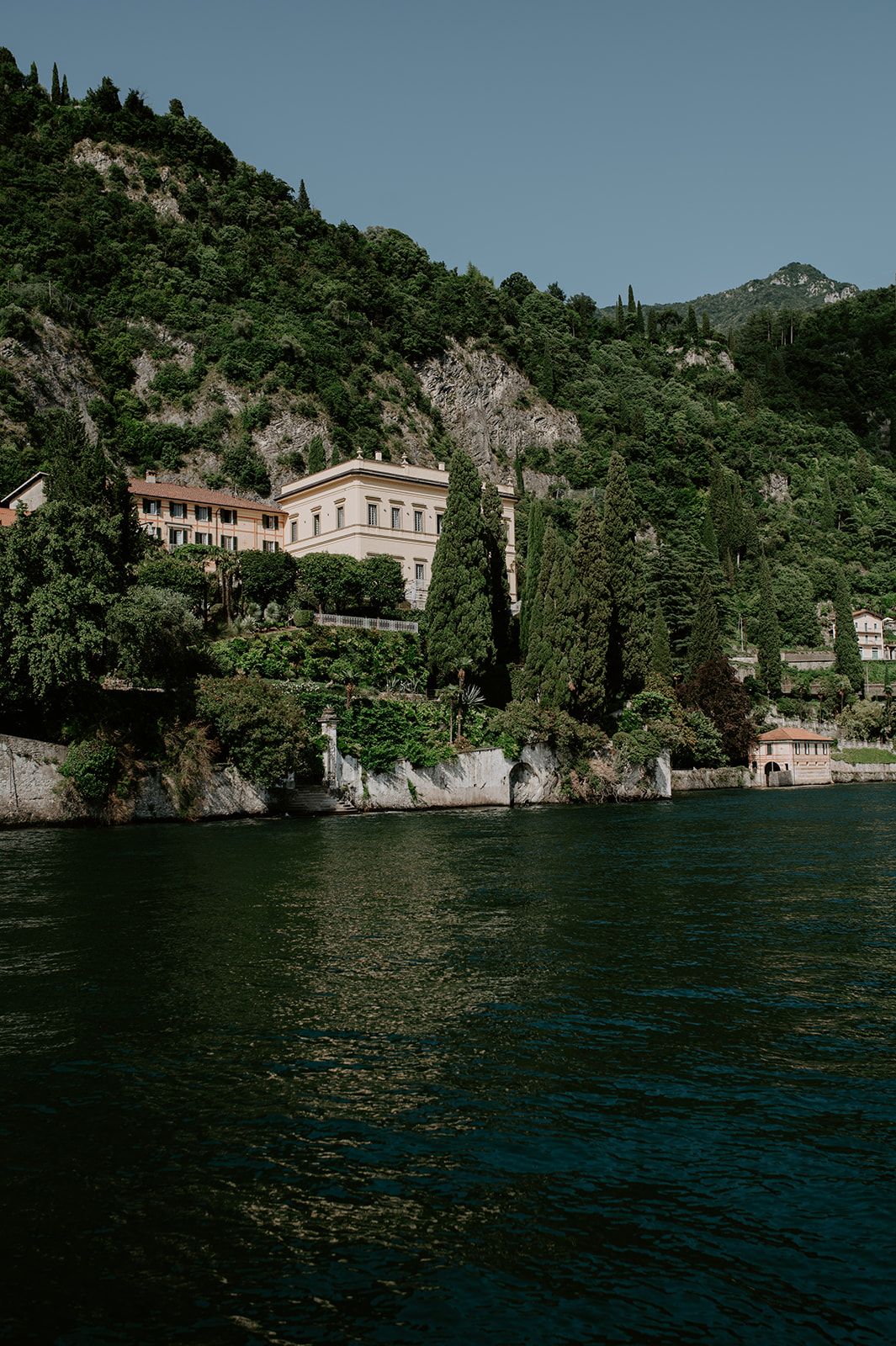 Historic lakeside villa nestled among cypress trees and mountains on Lake Como's shoreline.