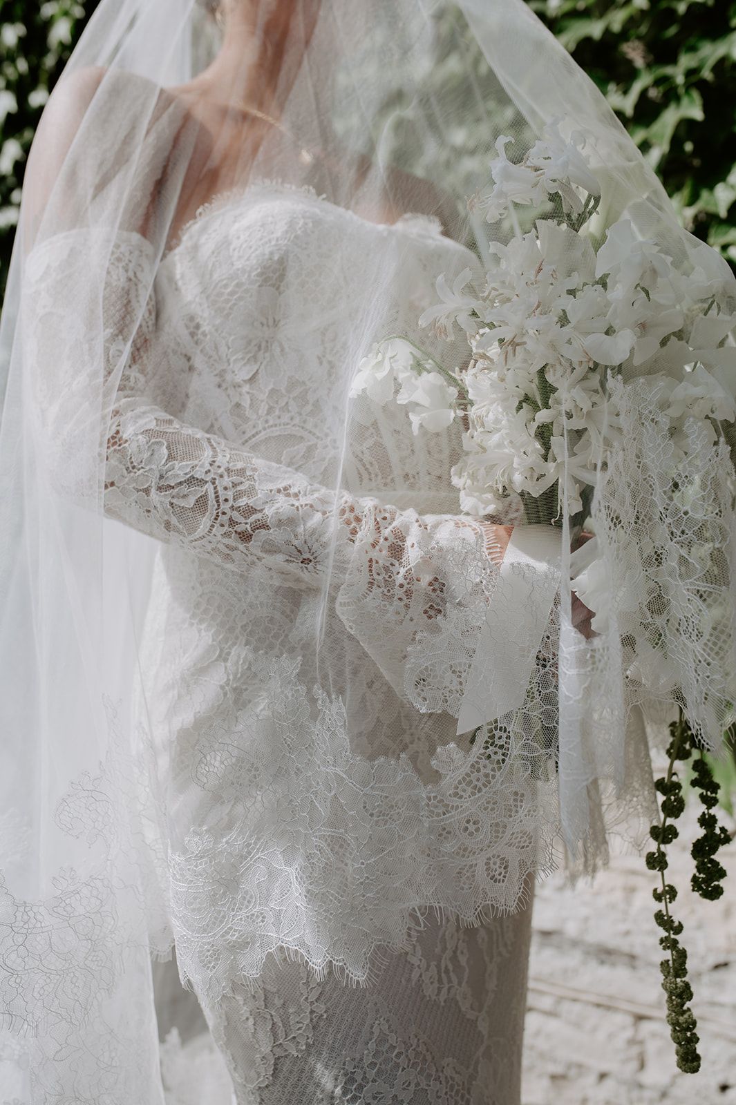 Delicate white lace wedding dress detail with ivy leaves in background.