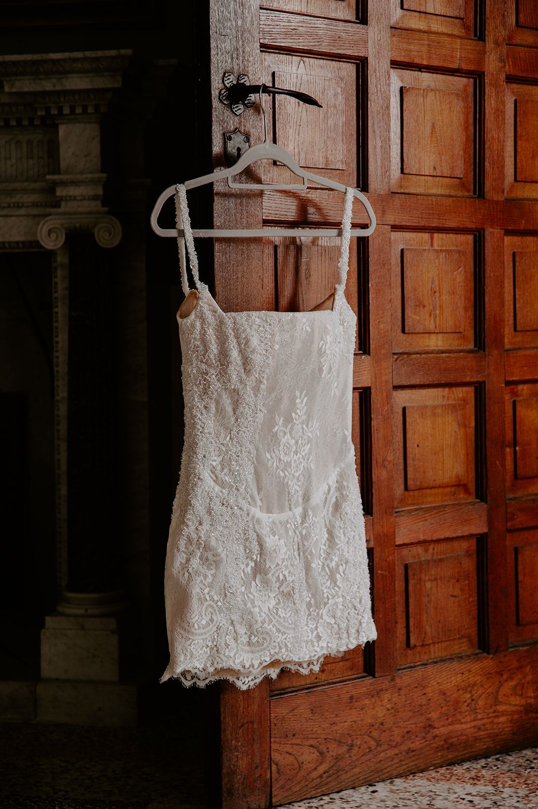 A white lace wedding dress hangs elegantly against a wooden paneled wall.