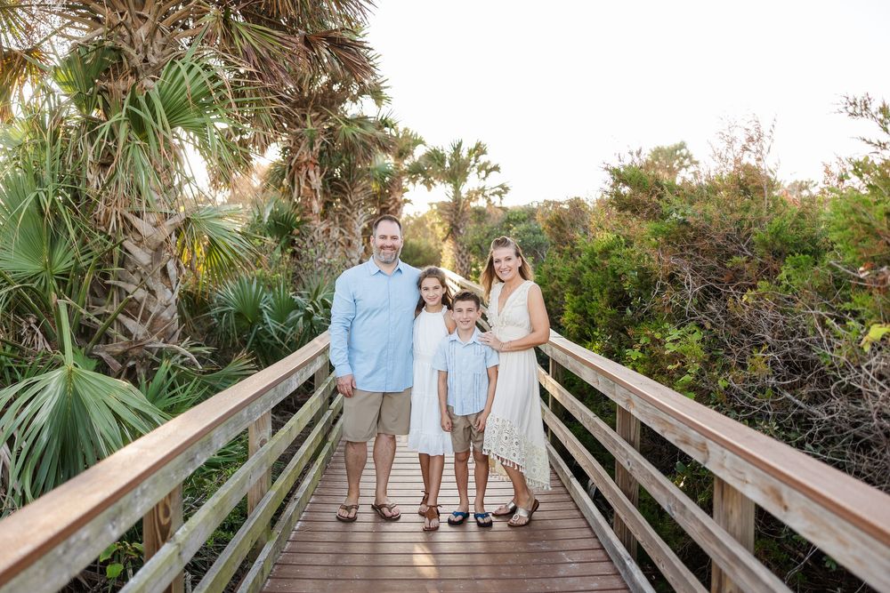 A family stands together on a wooden boardwalk surrounded by tropical palm trees and vegetation.