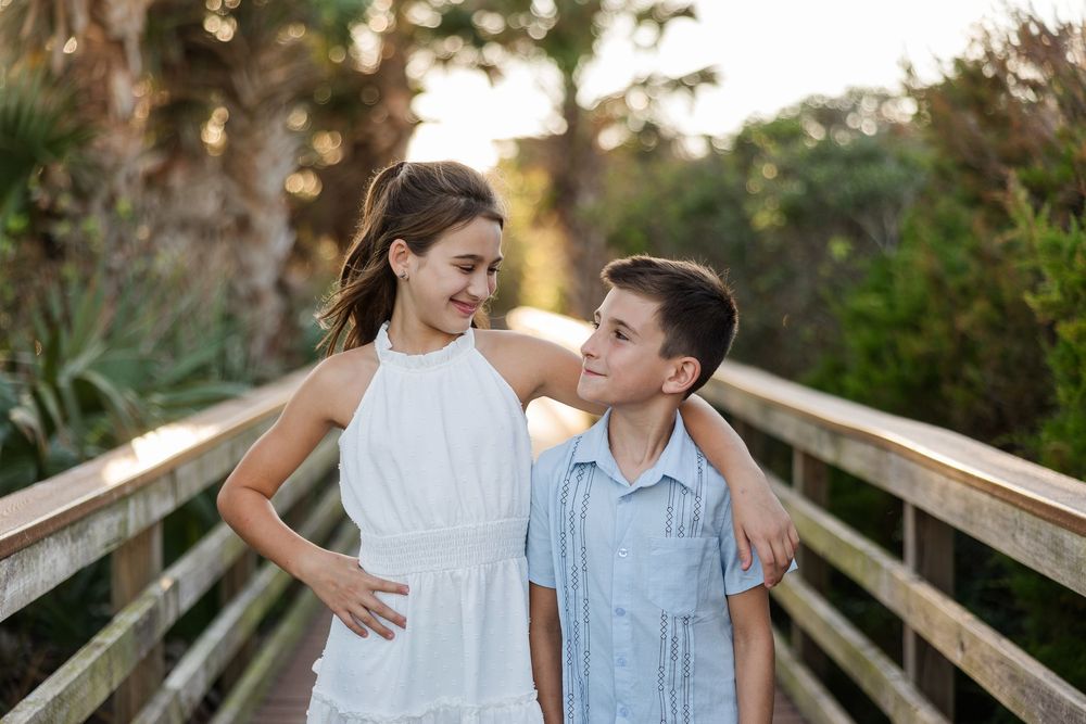 Two children share a sweet moment together on a wooden boardwalk at sunset.