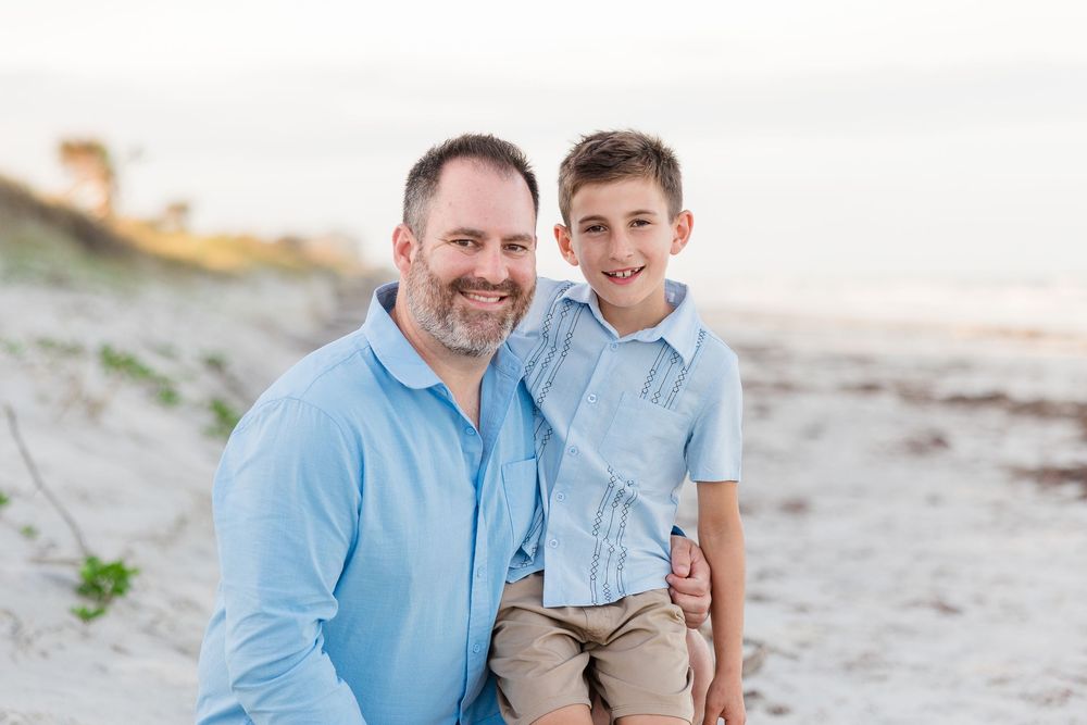 A father and son share a tender moment together on the beach at sunset.