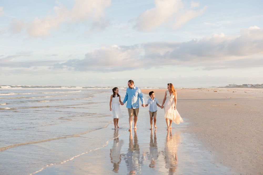 Family walking along the shoreline holding hands during golden hour at the beach.