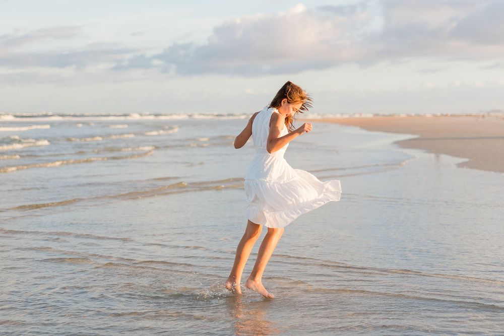 People running and playing in the shallow ocean waves during sunset.